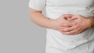 Person in a white shirt clutching their stomach with both hands, indicating abdominal pain or discomfort.